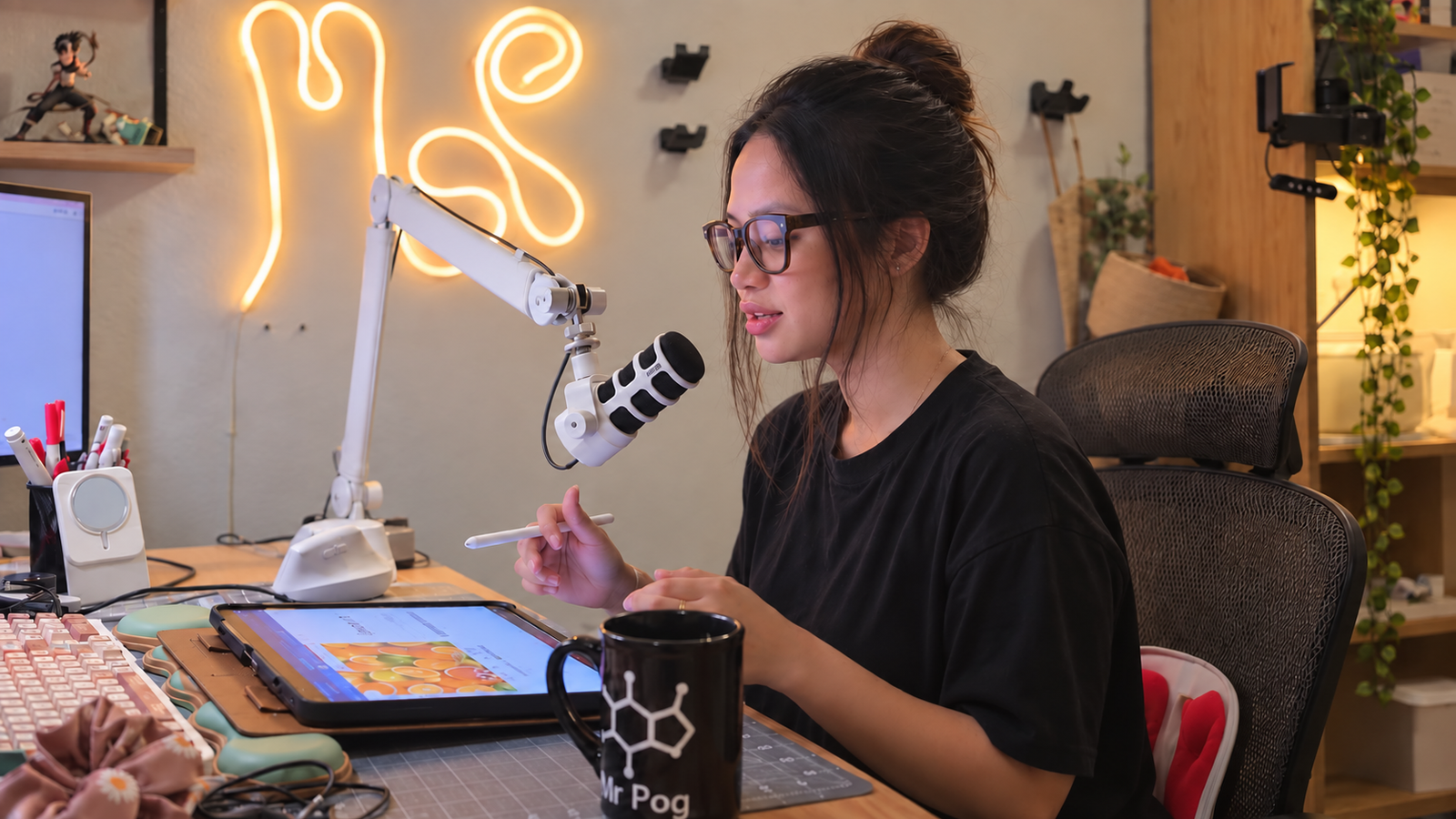 Adrianne Penullar at her desk — stylus in hand, chemistry mug, iPad, and amber neon sign